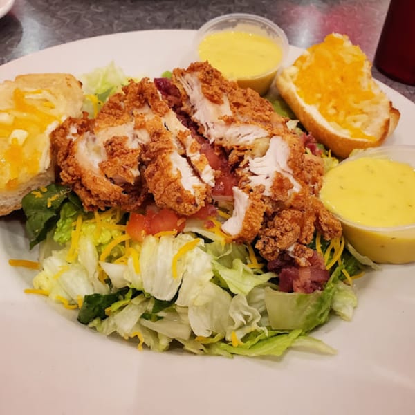 Crispy fried chicken salad with cheese, tomatoes, bacon, and two sides of dressing at RedEye Diner.