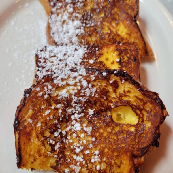 Three slices of golden-brown French toast, dusted with powdered sugar, on a white plate at RedEye Diner.