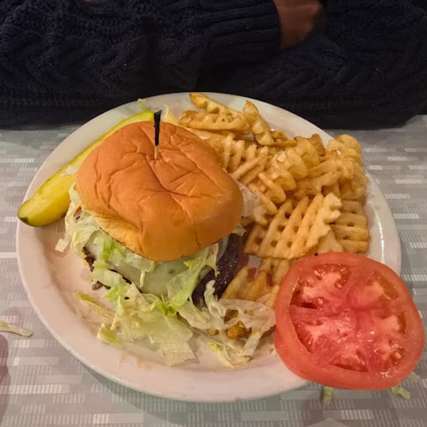 A RedEye Diner burger with waffle fries, a pickle spear, and a tomato slice on a white plate.