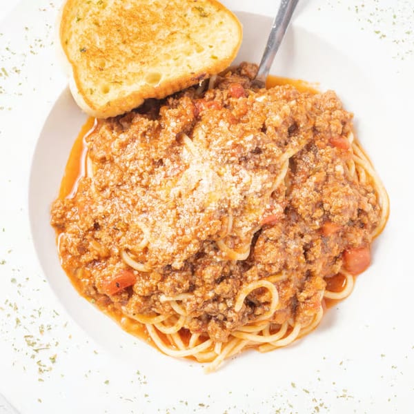 Spaghetti with meat sauce and grated cheese, served with a slice of garlic bread.