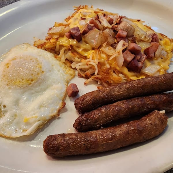 A diner breakfast with a fried egg, hash browns topped with cheese, onions, and ham, and three sausage links.